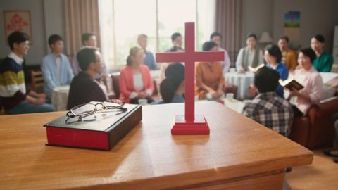 十字架和聖經在桌子上的近鏡頭，弟兄姊妹聚會的遠鏡頭