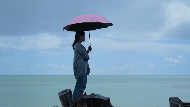 一個女人打着傘站在海邊，心情很沉重